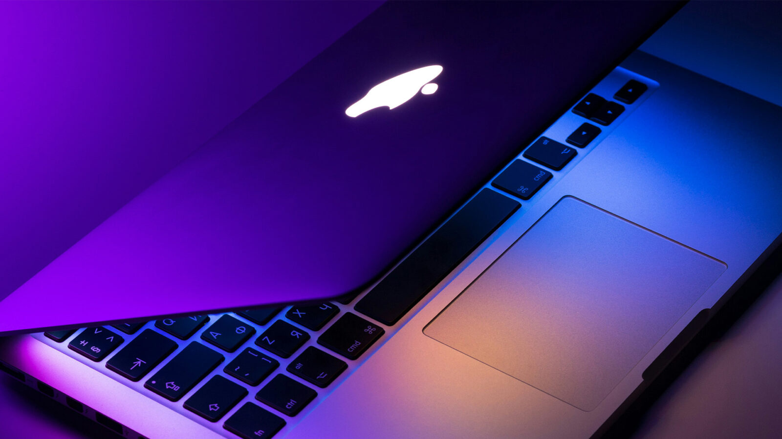 Half open Apple macbook with purple lighting.