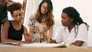 Three women of differing races at a table reviewing documents.