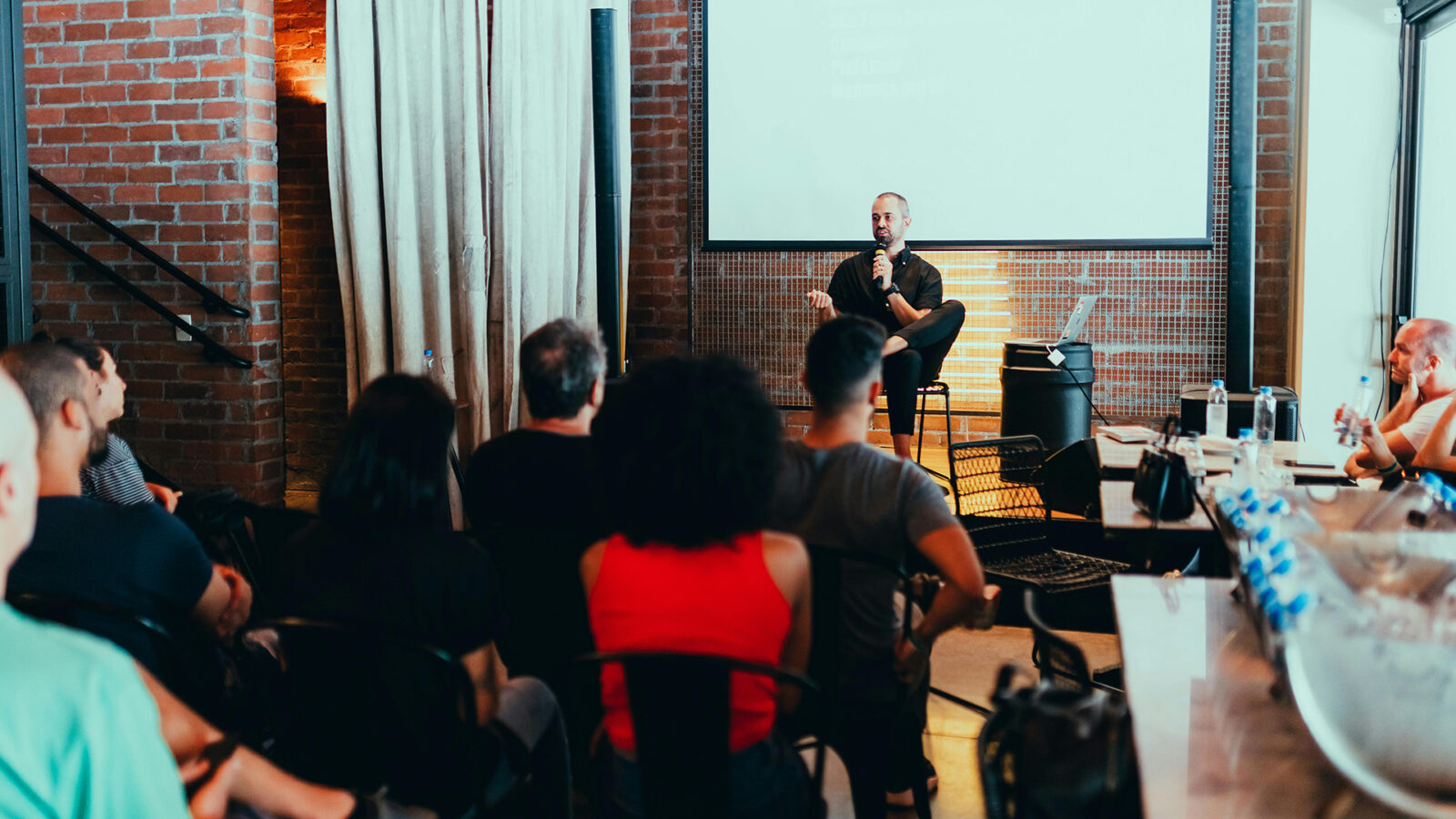 Man sitting on stage in a small venue in front of a crowd.