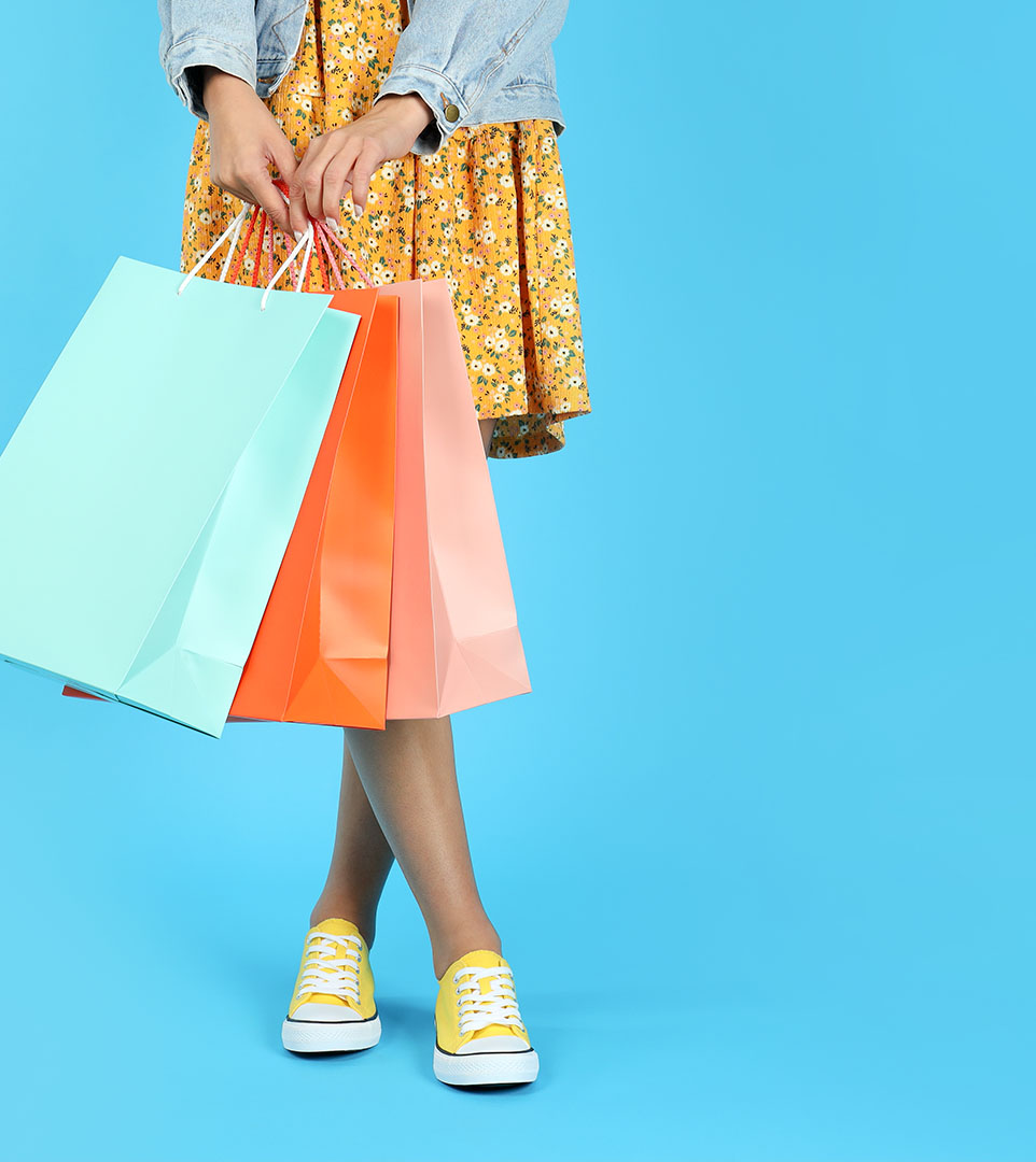 Woman in yellow flowery dress holding shopping bags.