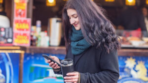 Woman holding phone and cup in a market