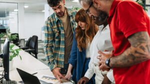 Diverse team working together, they are standing and looking at papers and a computer on a table.