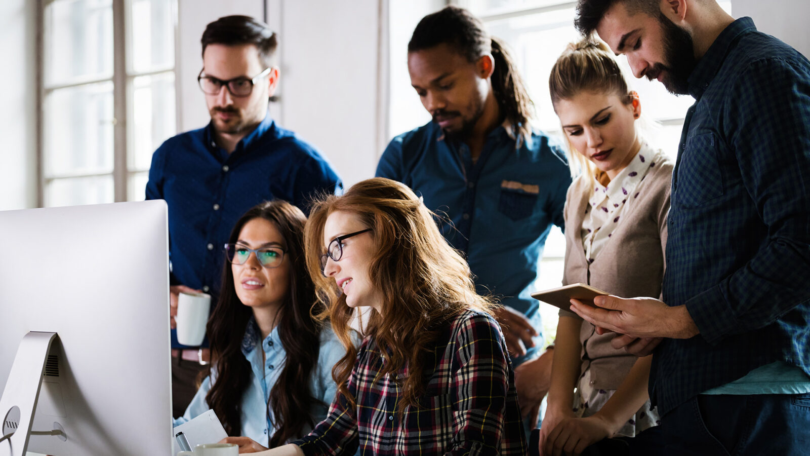 A group of collegues standing around a computer collaborating